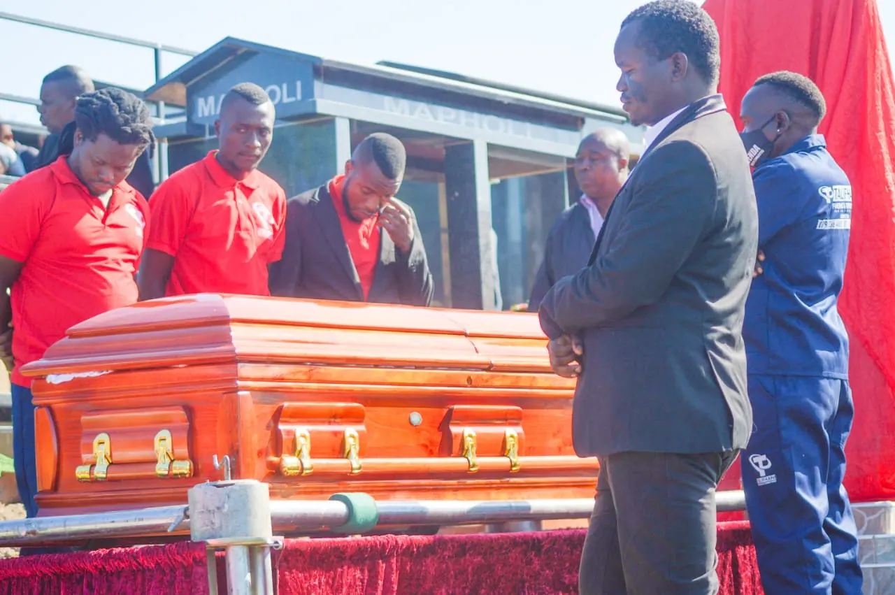 Talifhani team gathered respectfully around a coffin at the graveside