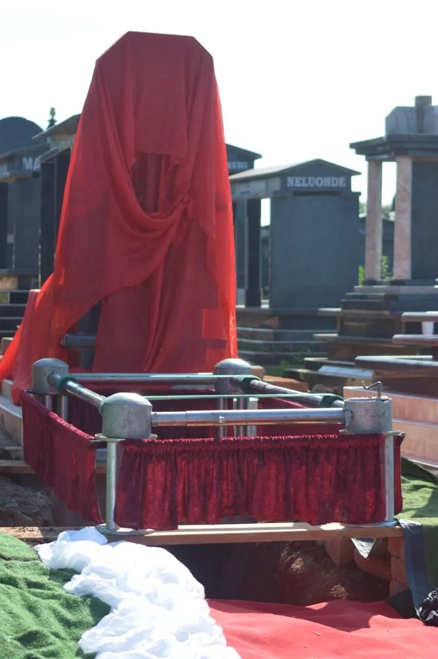 Graveside prepared with red draping and a covered memorial